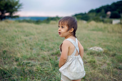 Boy in a beige light overalls walking on the field in the mountains in the summer evening alone