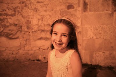 Portrait of cute happy girl standing against wall at night