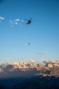 Airplane flying over snowcapped mountains against blue sky