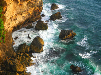 High angle view of sea waves splashing on rock formation by cliff