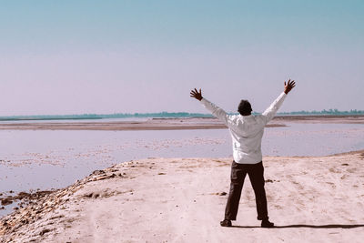 Rear view of man standing on a river bank against clear sky