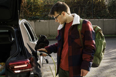 Man wearing backpack while charging electric car at station