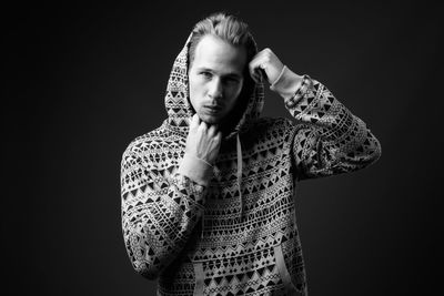 Portrait of young man standing against black background