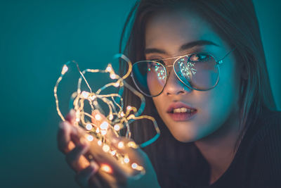 Close-up portrait of young woman holding illuminated string light