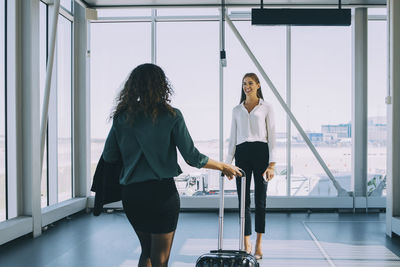 Smiling businesswoman looking at colleague walking in airport corridor