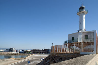 Lighthouse amidst buildings against clear blue sky