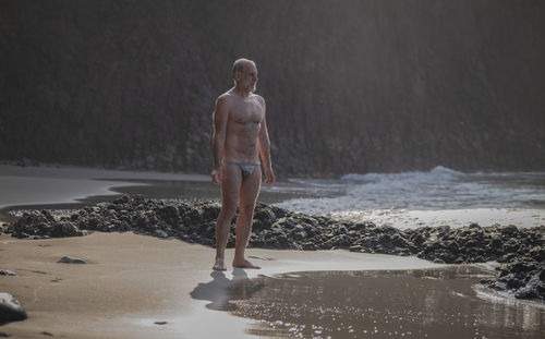 Full length of shirtless man with swimwear standing on beach