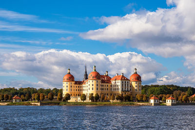 Buildings at waterfront against cloudy sky