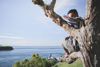 Man on rock by sea against sky