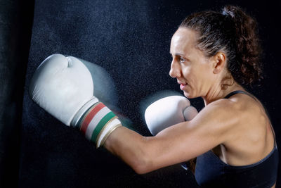 Female boxer punching bag against black background