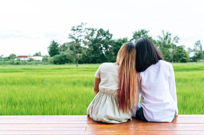 Rear view of women sitting on plants against sky