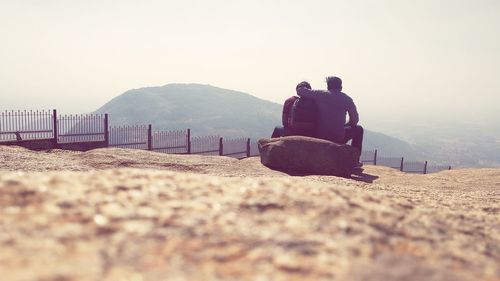 Rear view of people sitting on mountain against clear sky