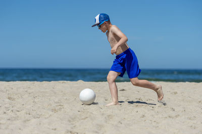 Boy kicking volleyball against sea