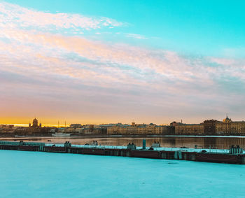Scenic view of river by city against sky during sunset