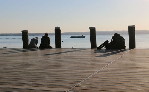 People sitting by sea against clear sky during sunset