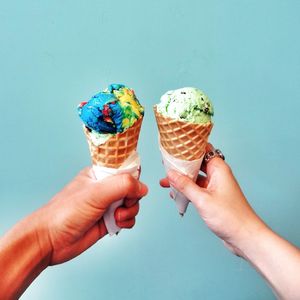 Cropped image of hands holding ice cream against blue background