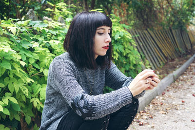 Woman sitting on footpath against plants