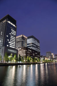 Illuminated buildings by river against sky at night