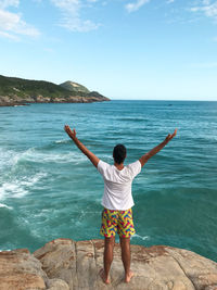 Rear view of man standing on rock by sea