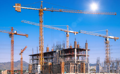 Low angle view of cranes against blue sky