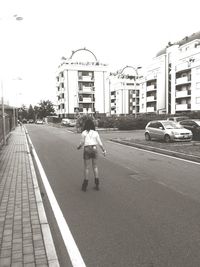 Rear view of man walking on road along buildings