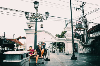People sitting on bridge against sky in city