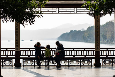 People sitting on railing by sea