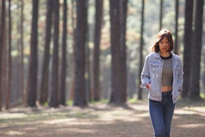 Full length of woman standing by tree trunk in forest