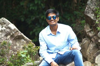 Portrait of smiling man sitting on rock in forest