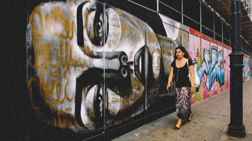 Portrait of woman standing by graffiti on wall