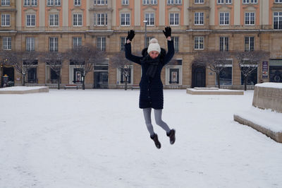 Young woman in mid-air over snow covered field against building