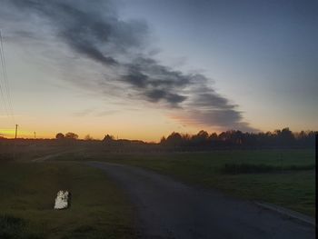 Road amidst field against sky during sunset