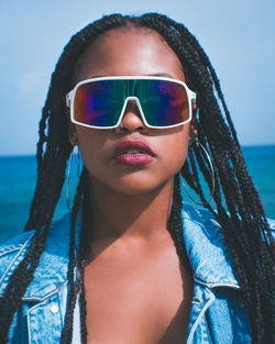 Portrait of young woman wearing sunglasses at beach against sky