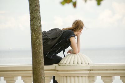 Woman sitting by sea against sky