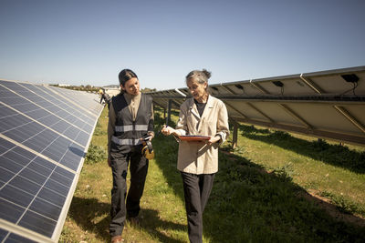 Senior female entrepreneur discussing with engineer while walking near solar panels during visit at power station