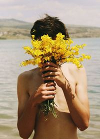 Midsection of young woman holding flower against sea