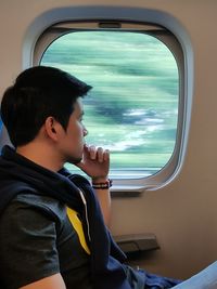 Side view of man looking through train window