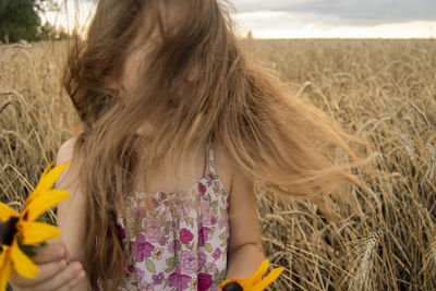 Girl with messy hair holding sunflowers on field