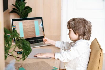 Rear view of boy using mobile phone at home