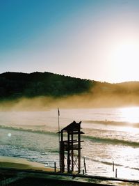 Silhouette lifeguard hut on beach against clear sky during sunset