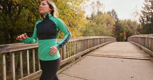 Young woman on running on footbridge against sky