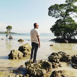 Man standing on rock by sea against sky