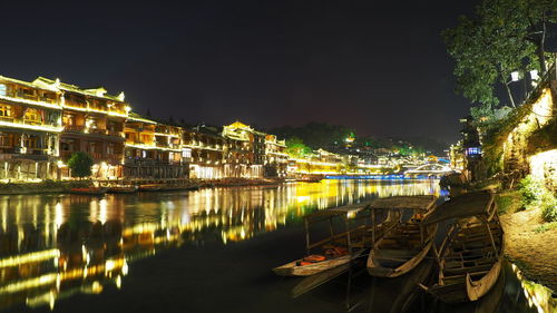 Boats moored in illuminated canal by buildings against sky at night