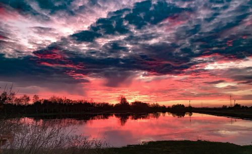 Scenic view of lake against dramatic sky during sunset