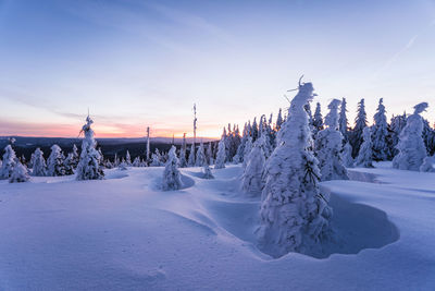 Snow covered landscape against sky during sunset