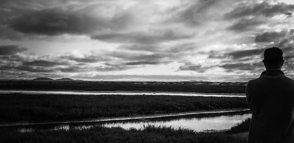 Rear view of man standing on land against cloudy sky