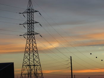 Low angle view of electricity pylon against sky at sunset