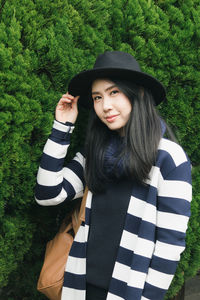 Portrait of smiling young woman standing against trees at park