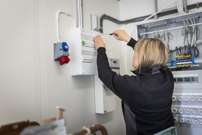 Blond female technician installing fuse box while working in control room of industry