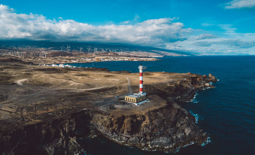 Lighthouse by sea against buildings